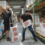 KEEPING STOCK: J.C. LeBarron, left, operations purchasing manager at Atlantic Paper & Supply, and Luis Deleon, a driver, work in the warehouse in Pawtucket stacking boxes.  PBN PHOTO/ELIZABETH GRAHAM