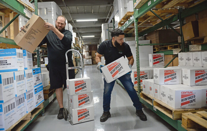 KEEPING STOCK: J.C. LeBarron, left, operations purchasing manager at Atlantic Paper & Supply, and Luis Deleon, a driver, work in the warehouse in Pawtucket stacking boxes.  PBN PHOTO/ELIZABETH GRAHAM