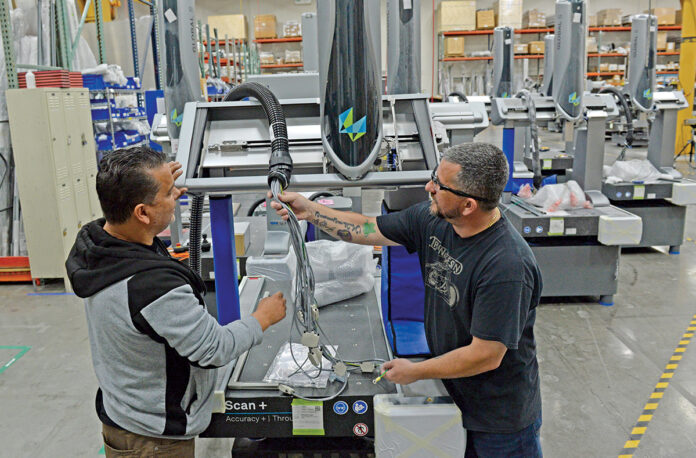 ALL WIRED UP: Joe Torres, left, a bridge assembly worker at Hexagon Manufacturing Intelligence Inc., and James Patnode, a machinist, work on the manufacturing floor at Hexagon’s North Kingstown facility. PBN PHOTO/ELIZABETH GRAHAM