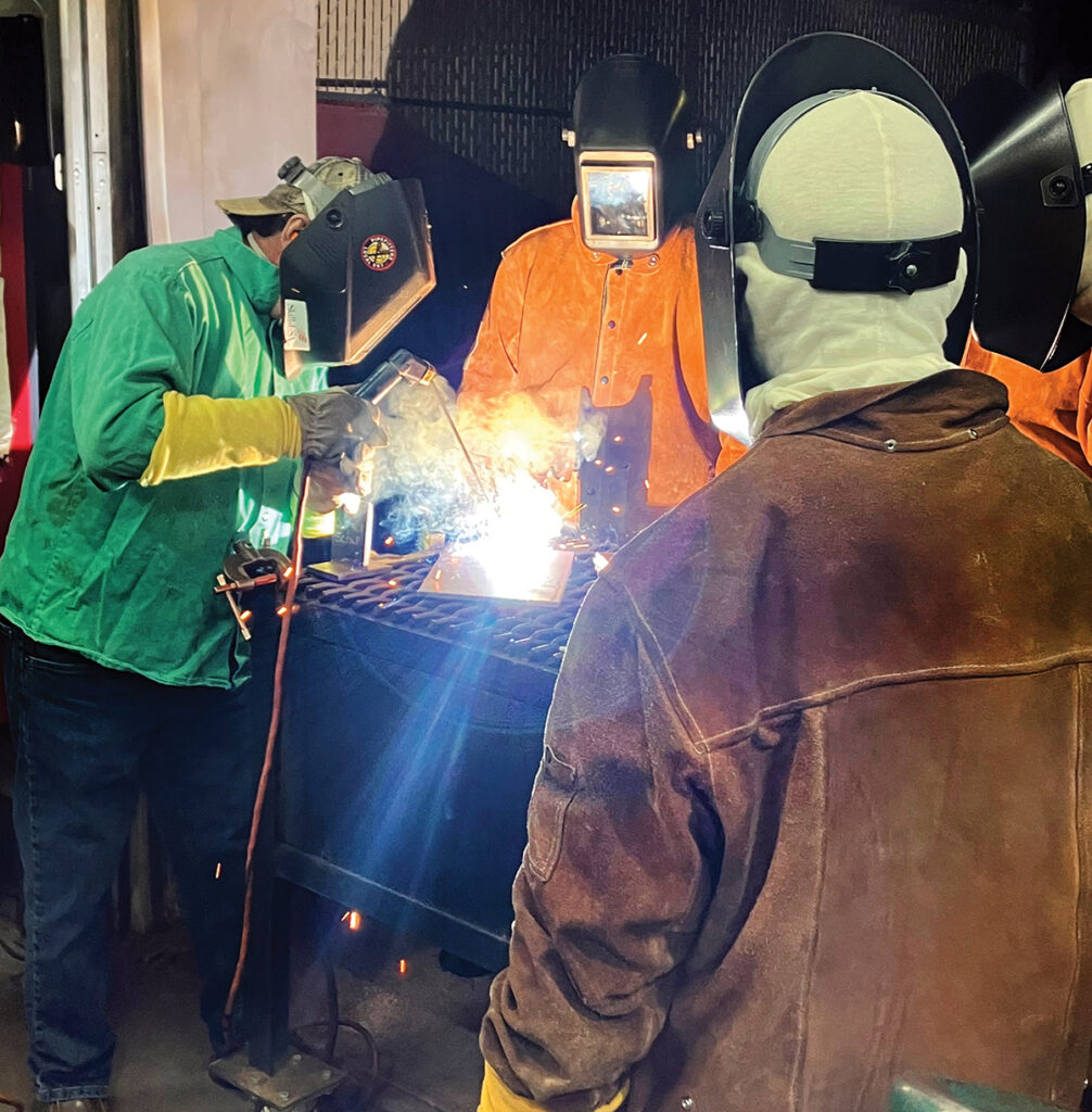 BRIGHT FUTURE: An instructor, left, shows a group of students welding techniques at the “Boat for Next Gen” program, a collaboration among Electric Boat, New England Institute of Technology, Community College of Rhode Island, the Westerly Education Center and the Southeastern New England Defense Industry Alliance.  COURTESY GENERAL DYNAMICS ELECTRIC BOAT