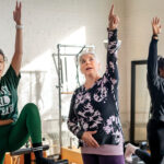REACHING FOR THE SKY: Mind 2 Body Fitness owner Maria ­Andresino, center, instructs Nicole Gonzalez, left, of Cumberland and Analy Lopes of East Providence during a Pilates class at her Providence studio. PBN PHOTO/MICHAEL SALERNO