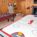 ALL ABOUT FUN: Allie Readyhough Shore, broker associate at Mott & Chace Sotheby’s International Realty, stands in a fully stocked game room in the basement of a home in South Kingstown. These types of amenities and much more are a big trend in high-end homes these days.  PBN PHOTO/­MICHAEL SALERNO