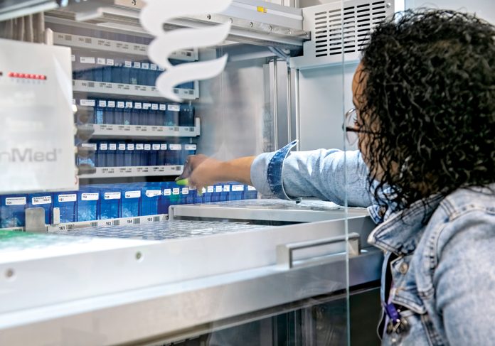 AI ASSIST: Pharmacy technician Nabile Bonagua reaches for medication from the SynMed XF, a pill-packing robot, at Horizon Pharmacy in Warwick. Horizon uses artificial intelligence to help it fill prescriptions, allowing pharmacists to focus on patients. PBN PHOTO/MICHAEL SALERNO