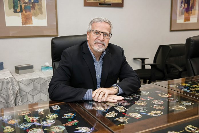 MEDALS OF HONOR: ChemArt Co. co-owner and President Dave Marquis sits at his desk that displays various medallions his Lincoln-based company produces. Much of those medallions support nonprofits and similar organizations.  PBN PHOTO / TRACY JENKINS