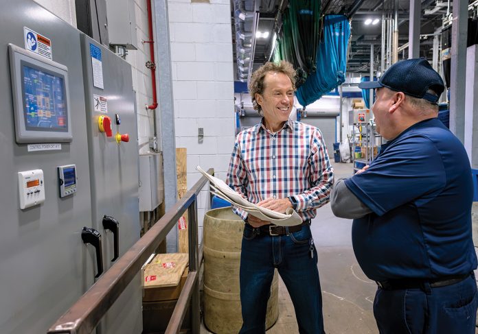 CHECKING UP: Michael Cahill, left, who owns BCX Energy Inc. and leads its air quality business unit, looks at the regenerative thermal oxidizer control panel installed at uniform service company Clean Uniforms and More! in New Bedford, one of BCX Energy’s clients. At right is Nino Valez, production supervisor at Clean Uniforms. PBN PHOTO/MICHAEL SALERNO