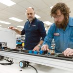 MANY USES: VR Industries Inc. CEO and President Brian Pestana, left, visits machine technician Brandon Roy on the factory floor of the Warwick-based electronic contract manufacturer, which focuses on making circuit boards for a variety of industries, including industrial, defense, medical and the blue economy.   PBN PHOTO/RUPERT WHITELEY