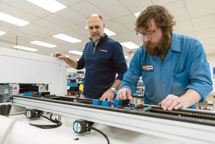 MANY USES: VR Industries Inc. CEO and President Brian Pestana, left, visits machine technician Brandon Roy on the factory floor of the Warwick-based electronic contract manufacturer, which focuses on making circuit boards for a variety of industries, including industrial, defense, medical and the blue economy.   PBN PHOTO/RUPERT WHITELEY