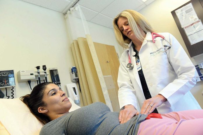 EASING THE BURDEN: Erica Ogni, right, an adult-gerontology nurse practitioner, gives a checkup to patient Lexi Palumbo at South County Health in East Greenwich. As the number of local doctors declines, nurse practitioners are increasingly seeing more patients. PBN FILE PHOTO/­ELIZABETH GRAHAM