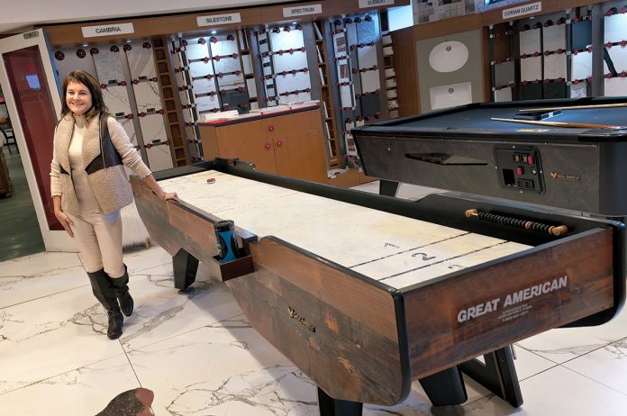 TABLE GAMES: Tracey Beck, co-owner and chief operating officer of The Beck Cos., shows off a shuffleboard table and a pool table, both designed and built by Great American Recreation Equipment Inc., one of six companies under The Beck Cos. umbrella that produces its products at the manufacturer’s 85,000-square-foot facility in North Smithfield. PBN PHOTO/MICHAEL SALERNO