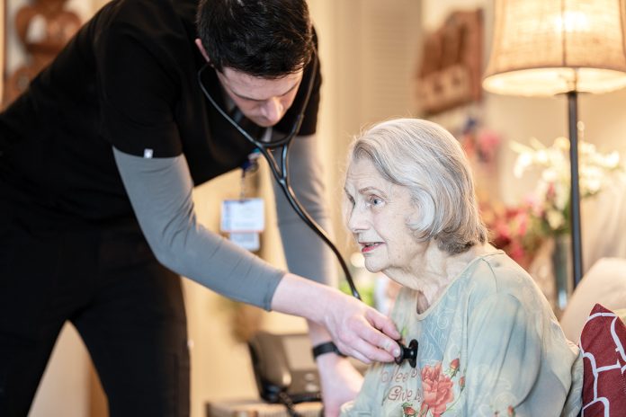 HOUSE CALL: Dr. Tyler Weisberger, left, who works for Kent County Memorial Hospital’s Hospital at Home program, examines Doris Witt at her Warwick home. Witt was admitted to Kent in early March after experiencing symptoms from her congestive heart failure. The Hospital at Home program allowed her to be discharged early but still receive hospital-level care.  COURTESY CARE NEW ENGLAND HEALTH SYSTEM