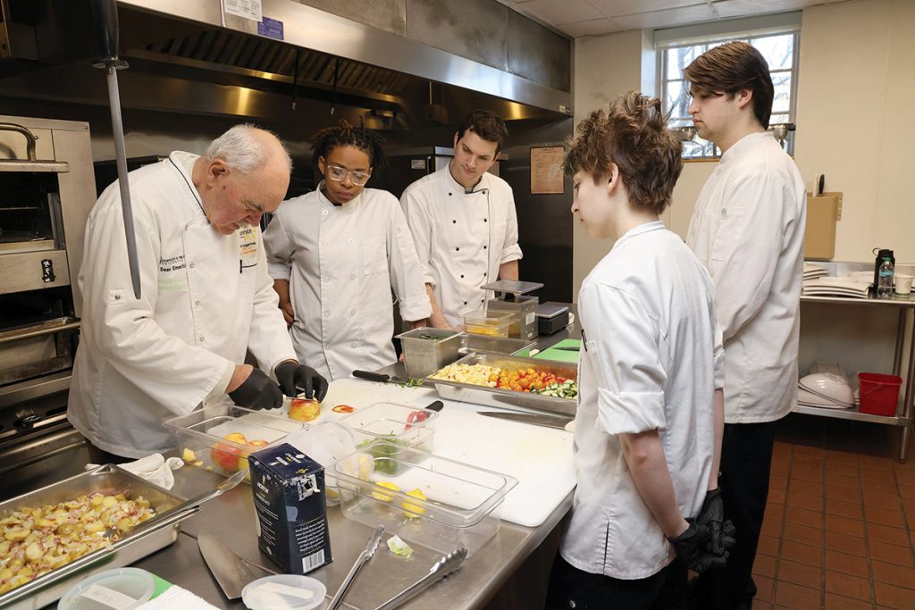 MASTER CHEF: Karl J. Guggenmos, left, a certified global master chef, works with Community College of Rhode Island culinary students. Guggenmos is helping to develop a new associate in arts degree in culinary craftsmanship at the college’s Newport campus beginning in fall 2025.  COURTESY COMMUNITY COLLEGE OF RHODE ISLAND