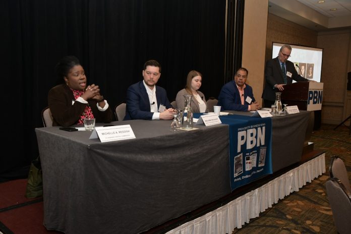 cannabissummi2025 MICHELLE A. REDDISH, left, administrator for the R.I. Cannabis Commission, speaks at Providence Business News' The Business of Cannabis Summit at the Providence Marriott on Thursday. Also on the panel is, from left, Benjamin L. Rackliffe, partner of Pannone Lopes Devereaux & O’Gara LLC; Sasha Gorski, co-owner of Talaria LLC; and Ronald Crosson II, executive director of Urban Ventures Inc. and chairman and social equity officer of the R.I. Cannabis Advisory Board. PBN Editor Michael Mello, standing, moderates. / PBN PHOTO/MIKE SKORSKI