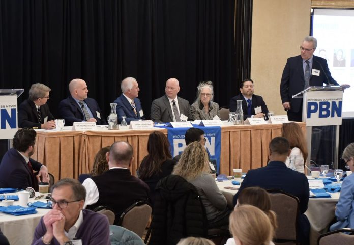 GREGORY MERCURIO, third from left, speaks during a panel discussion at Providence Business News' Health Care Summit and Health Care Heroes Awards event on Wednesday morning at the Providence Marriott. Mercurio is senior vice president of radiation oncology at American Shared Hospital Services and CEO of Precision Radiation Oncology of Rhode Island. Also on the panel is, from left, Dr. Michael Wagner, CEO and president of Care New England Health System; Joseph Trunzo, founding associate director of Bryant University's School of Health and Behavioral Sciences and a professor of psychology; Peter Marino, CEO and president of Neighborhood Health Plan of Rhode Island; Linda Hurley, CEO and president of CODAC Behavioral Healthcare; and Dr. Raj Hazarika, chief medical officer for commercial products at Point32Health. PBN Editor Michael Mello, standing, moderates. / PBN PHOTO/MIKE SKORSKI