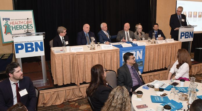 GROUP EFFORT: Peter Marino, fourth from the left, CEO and president of Neighborhood Health Plan of Rhode Island, speaks during a panel discussion at Providence Business News’ Health Care Summit and Health Care Heroes Awards event on April 2 at the Providence Marriott. Also on the panel are, from left, Dr. Michael Wagner, CEO and president of Care New England Health System; Joseph Trunzo, founding associate director of Bryant University’s School of Health and Behavioral Sciences and a professor of psychology; Gregory Mercurio, senior vice president of radiation oncology at American Shared Hospital Services and CEO of Precision Radiation Oncology of Rhode Island; Linda Hurley, CEO and president of CODAC Behavioral Healthcare; and Dr. Raj Hazarika, chief medical officer for commercial products at Point32Health Services Inc. PBN Editor Michael Mello, standing, moderates.  PBN PHOTO/MIKE SKORSKI