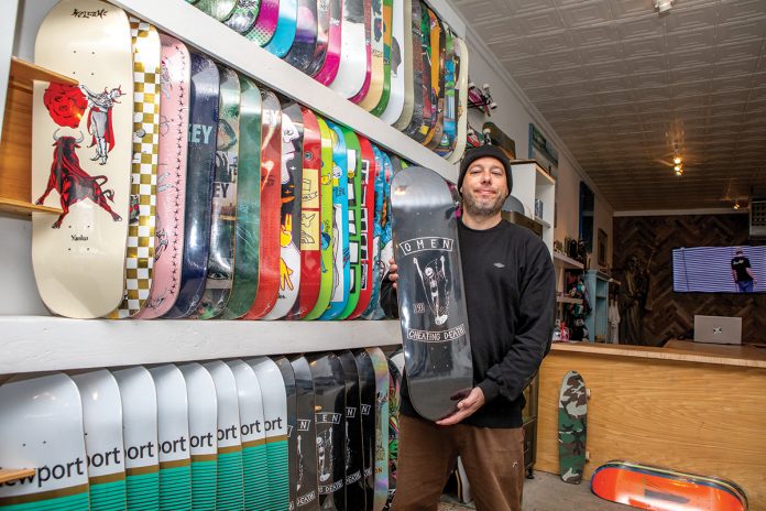 ROLLING ALONG: Cheyne Cousens moved back from California in 2023 to run his father’s Elemental Surf and Skate shop in Middletown, which he rebranded Omen after an idea that began as a hobby in 2014 with printed-up T-shirts with logos and artwork he personally designed.  PBN PHOTO/KATE WHITNEY LUCEY