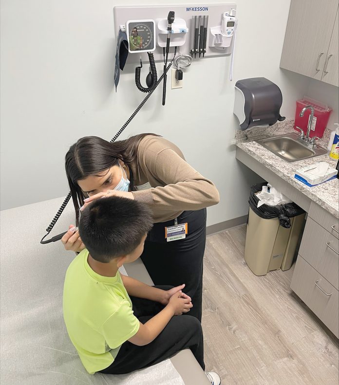 A CLOSE LOOK: Carolina Carrillo, a Warren Alpert Medical School student, conducts a health examination of a Calcutt Middle School student at the SMART Plus clinic at Calcutt in Central Falls. Medical students also serve as mentors for middle schoolers interested in the field of health care.  COURTESY WARREN ­ALPERT MEDICAL SCHOOL