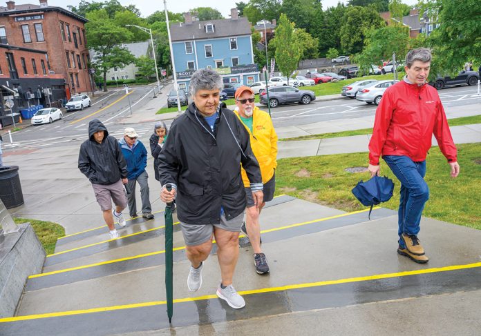 GOING ON FOOT: Sonia Rodriguez, holding the green umbrella, of Smithfield leads the “Walk with a Doc” at South Main Street in Providence in June. Although there was no doctor on this particular walk and it was threatening to rain, the participants forged ahead because the health-related program has also become a social exercise.  PBN PHOTO/MICHAEL SALERNO