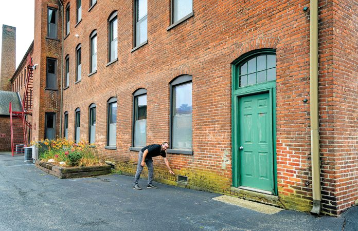 ON THE MARK: Richard Grundy, CEO and president of AVTECH Software Inc., indicates the level of floodwater at Cutler Mill in Warren, where AVTECH’s offices are located.  PBN PHOTO/MICHAEL SALERNO