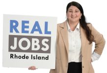 the prop Alyssa Alvarado holds the  Real Jobs Rhode Island sign, symbolizing her decade-plus time working to grow the state’s workforce development program.