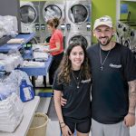 ALL IN THE FAMILY: James Manzo and fiancée Vanessa Fonseca, co-owners of Cleanville Laundromat in Smithfield, with laundry attendant Maggi Fonseca folding clothes in the background.  PBN PHOTO/MICHAEL SALERNO