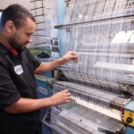 Meet the Makers: DaRosas weaving an impactful legacy in Pawtucket TIGHTENING UP: North East Knitting Inc. lead mechanic José Dos Reis adjusts fabric in one of the machines at the Pawtucket manufacturer.
PBN PHOTO/TRACY JENKINS