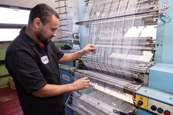 TIGHTENING UP: North East Knitting Inc. lead mechanic José Dos Reis adjusts fabric in one of the machines at the Pawtucket manufacturer. PBN PHOTO/TRACY JENKINS