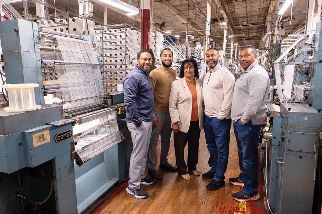 FAMILY TIES: North East East Knitting Inc. co-founder and President Rosalie DaRosa, middle, is surrounded by, from left, her son Michael DaRosa; her grandson Marcus DaRosa, who now oversees the business; and her sons Alex and Eric DaRosa at the company’s manufacturing facility in Pawtucket. PBN PHOTO/TRACY JENKINS