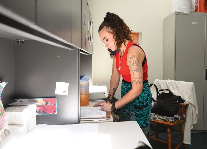 PAPERWORK: Rivka Reynolds, a peer recovery counselor with Thrive Behavioral Health Inc., fills out some paperwork in her organization’s West Warwick office. PBN PHOTO/PAUL SPETRINI