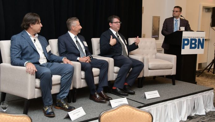 DOUGLAS ALEXANDER, seated at right, director of the Institute for Cybersecurity & Emerging Technologies at Rhode Island College, speaks during a panel discussion at Providence Business News' Cybersecurity, AI & Tech Summit at Crowne Plaza Providence-Warwick. Alexander was joined on the panel by, from left, David Phillips, chief information security officer at OSHEAN Inc., and Rick Norberg, CEO at Vertikal6 Inc. Guest moderator is Norman Duquette, standing, senior vice president at Starkweather & Shepley Insurance Brokerage Inc. / PBN PHOTO/MIKE SKORSKI