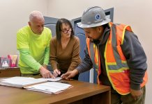 GAME ­PLANNING: Lori Manni, center, president of Capital City Construction & Management Services Inc., goes over documents with Al DeRobbio, left, project supervisor, and Oliver Carias, operating engineer of Local 57, at the company’s Cranston office. PBN PHOTO/­MICHAEL SALERNO