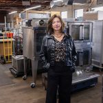 GOT ­SOMETHING COOKING:  Lisa Raiola, founder and president of Hope & Main, stands among some of the kitchen equipment that will be put to use at the yet-to-be-completed new food business incubator, West End Kitchens, in Providence. It is set to open around June.  PBN PHOTO/TRACY JENKINS