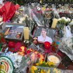 FLOWERS AND CANDLES surround photos of Mukhammad Aziz Umurzokov, an 18-year-old freshman from Brandermill, Va., and Ella Cook, a 19-year-old sophomore from a suburb of Birmingham, Ala., in front of a Brown University gate in Providence on Dec. 17. Both were killed in the campus shooting on Dec. 13. / AP FILE PHOTO/LEAH WILLINGHAM