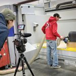 ACTION: Composite manufacturer Moore Brothers Co. in Bristol uses social media to market its business. Floor technician and multimedia creator Jacob Rapoza, left, records computer numerical control programmer and operator Benjamin Calssen as he works on the CMS Ares 5 axis CNC Gantry machine. PBN PHOTO/MICHAEL SALERNO