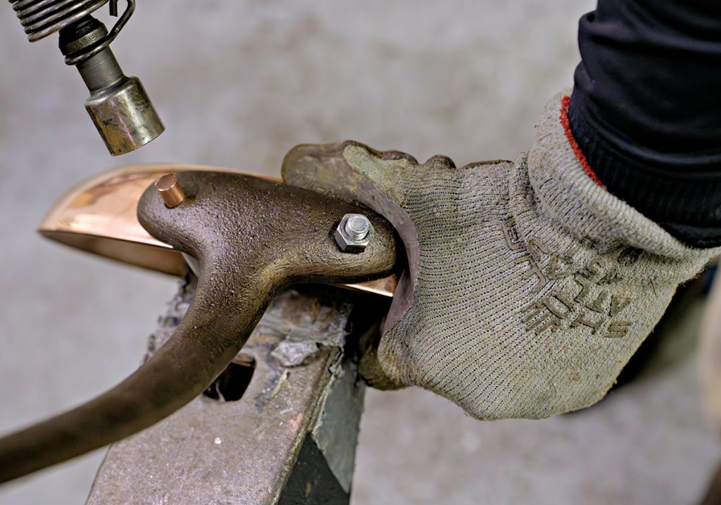 GETTING ATTACHED: A worker at ­Duparquet Copper Cookware prepares to rivet a handle to a piece of cookware.  PBN PHOTO/MICHAEL SALERNO