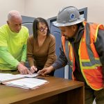 GAME ­PLANNING: Lori Manni, center, president of Capital City Construction & Management Services Inc., goes over documents with Al DeRobbio, left, project supervisor, and Oliver Carias, operating engineer of Local 57, at the company’s Cranston office. PBN FILE PHOTO/­MICHAEL SALERNO