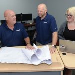 FAR REACH: Avidex Industries LLC serves clients worldwide. From left, Bob Mathews, senior account executive; Thomas Ward, senior project manager; and Dominique Perrin, project coordinator, work on blueprints in Warwick.  PBN PHOTO /ELIZABETH GRAHAM