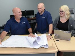 Warwick AV firm goes global: Avidex FAR REACH: Avidex Industries LLC serves clients worldwide. From left, Bob Mathews, senior account executive; Thomas Ward, senior project manager; and Dominique Perrin, project coordinator, work on blueprints in Warwick.
PBN PHOTO /ELIZABETH GRAHAM