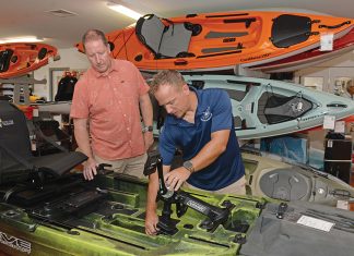 CHUGGING ALONG: Matt Bosgraaf, right, owner of the Kayak Centre in North Kingstown, adjusts the pedal drive system on a fishing kayak in the store’s showroom. With him is John Van Ness, the store’s product specialist. Bosgraaf says the business is growing, helped by the recent acquisition of a kayak rental business.  PBN PHOTO/­ELIZABETH GRAHAM