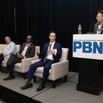 CHRISTOPHER PARISI, standing at right, founder and CEO of Trailblaze Marketing and vice chair of the Rhode Island AI Task Force, moderates a panel discussion during Providence Business News' 2026 Cybersecurity & AI Tech Summit on Thursday morning at the Crowne Plaza Providence-Warwick. Also on the panel, from right, are Seth Kolker, interim director of Rhode Island’s AI Hub; Arnell Milhouse, co-founder and CEO of yconic AI; and Robert Paradise, founder and CEO of Attain Technology. PBN PHOTO/MIKE SKORSKI