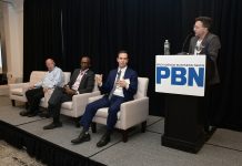 CHRISTOPHER PARISI, standing at right, founder and CEO of Trailblaze Marketing and vice chair of the Rhode Island AI Task Force, moderates a panel discussion during Providence Business News' 2026 Cybersecurity & AI Tech Summit on Thursday morning at the Crowne Plaza Providence-Warwick. Also on the panel, from right, are Seth Kolker, interim director of Rhode Island’s AI Hub; Arnell Milhouse, co-founder and CEO of yconic AI; and Robert Paradise, founder and CEO of Attain Technology. PBN PHOTO/MIKE SKORSKI