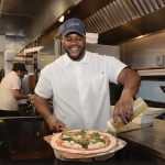CHEERFUL CHEF: ­Cedrick Almonacy, sous chef at Celeste restaurant in Narragansett, puts the finishing touches on a pizza. Almonacy said he has enjoyed cooking since childhood. PBN PHOTO/ELIZABETH GRAHAM