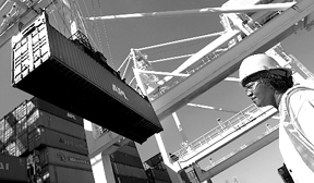 Worker at a container terminal in the Port of Oaklandwatches a crane load a cargo ship. Worker at a container terminal in the Port of Oakland<br>watches a crane load a cargo ship.