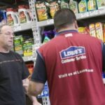 AT LOWE'S in Natick, Mass., store manager Brian Rebello, right, yesterday explains termite products to customer Joe O'Brien. The chain has lowered its annual earnings forecast, citing the real estate slump that continues to pare home-improvement sales. / 