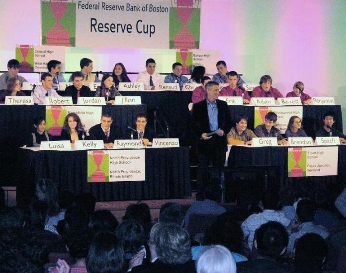 TV HOST BILLY COSTA, of New England Cable News, stands between the Rhode Island team, front left, and the team from Vermont at the Federal Reserve Bank of Boston during the 2007 Reserve Cup competition. Behind them are teams representing Connecticut, Massachusetts, Maine and New Hampshire. / 