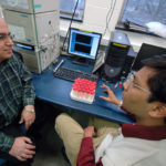 KEYKAVOUS PARANG, left, a professor at the University of Rhode Island, talks with graduate student Kitesh K. Agarwal as they test an anti-viral substance for purity. /