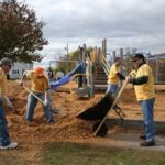 ADVANCED FINANCIAL SERVICES employees place woodchips for safety surfacing beneath the playground equipment at Abbot Court in Fall River. The company dedicates one work day per year to volunteer efforts. / 