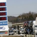 TRAFFIC ON I-95 passes a sign listing gasoline prices at a convenience store in Newton, Mass. / 