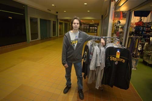 STEEL CURTAIN: Once surrounded by other shops, First Place Sports in Warwick’s Rhode Island Mall now sits adjacent to gated vacant storefronts. Above, owner Frank Silva poses with gear he
discounted in advance of the Super Bowl. / STEEL CURTAIN: Once surrounded by other shops, First Place Sports in Warwick’s Rhode Island Mall now sits adjacent to gated vacant storefronts. Above, owner Frank Silva poses with gear he
discounted in advance of the Super Bowl. /