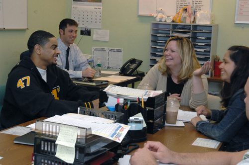 SERVING WITH HONOR: Tides Family Services caseworkers, from left, at table: Robert Reyes, Chantelle Rotolo, Vanessa DeLeon, and Greg D'Ambrea. At desk in rear is supervisor Patrick Costello. / SERVING WITH HONOR: Tides Family Services caseworkers, from left, at table: Robert Reyes, Chantelle Rotolo, Vanessa DeLeon, and Greg D'Ambrea. At desk in rear is supervisor Patrick Costello. /