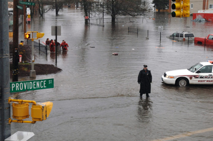 OFFICER PATRICK KELLY directs traffic away from River Street in West Warwick on Tuesday as firefighters evacuate residents from flooded homes. / OFFICER PATRICK KELLY directs traffic away from River Street in West Warwick on Tuesday as firefighters evacuate residents from flooded homes. /